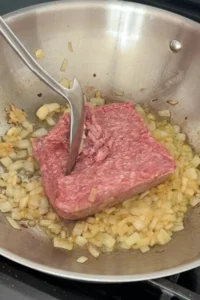 Ground pork added to sautéed onions and garlic in a skillet.