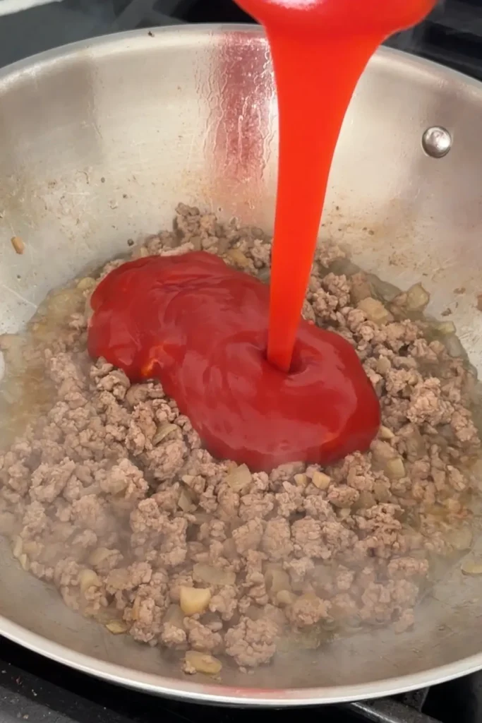 Tomato sauce being poured over cooked ground pork in a pan.