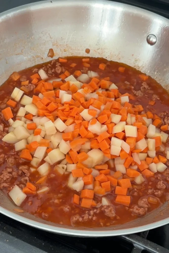 Diced potatoes and carrots added to ground pork in tomato sauce.