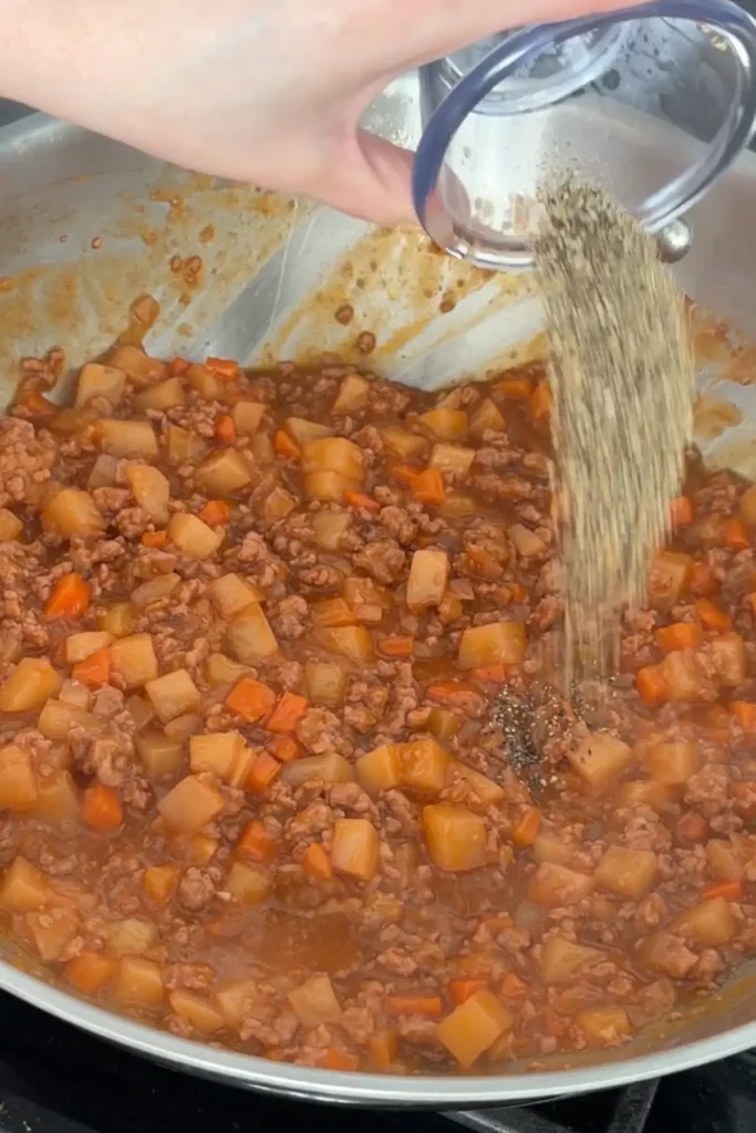 Black pepper being sprinkled into pork picadillo mixture.