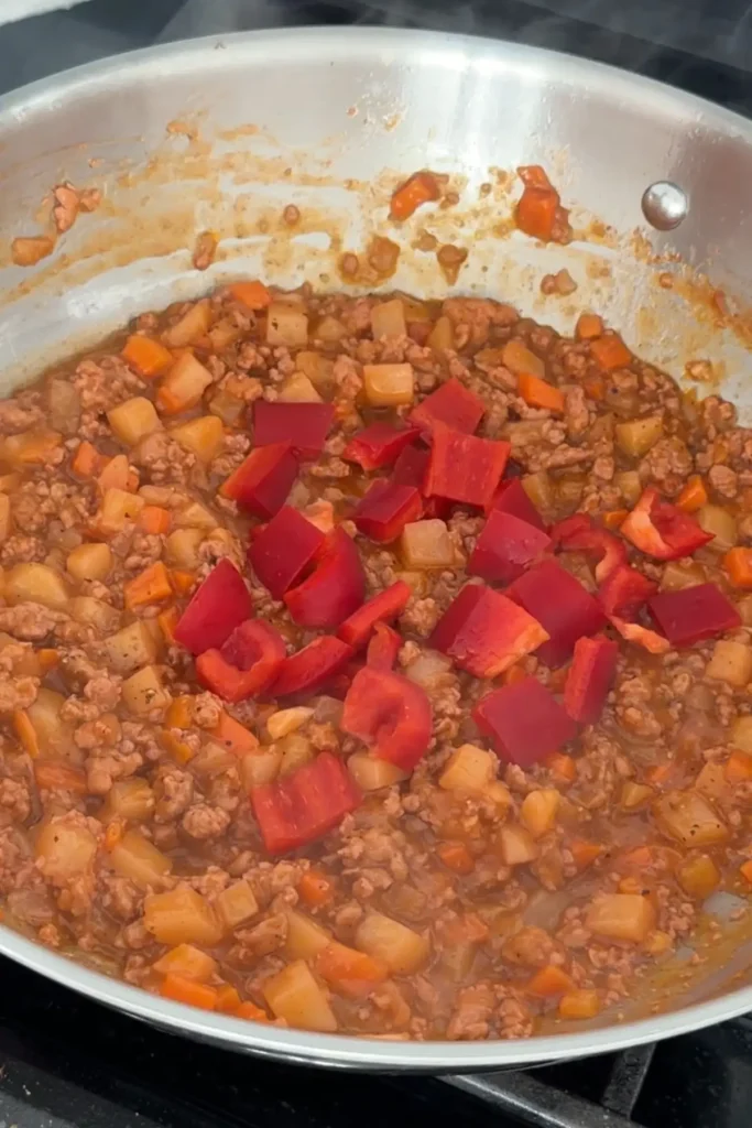 Diced red bell peppers added to simmering pork and vegetable mixture.