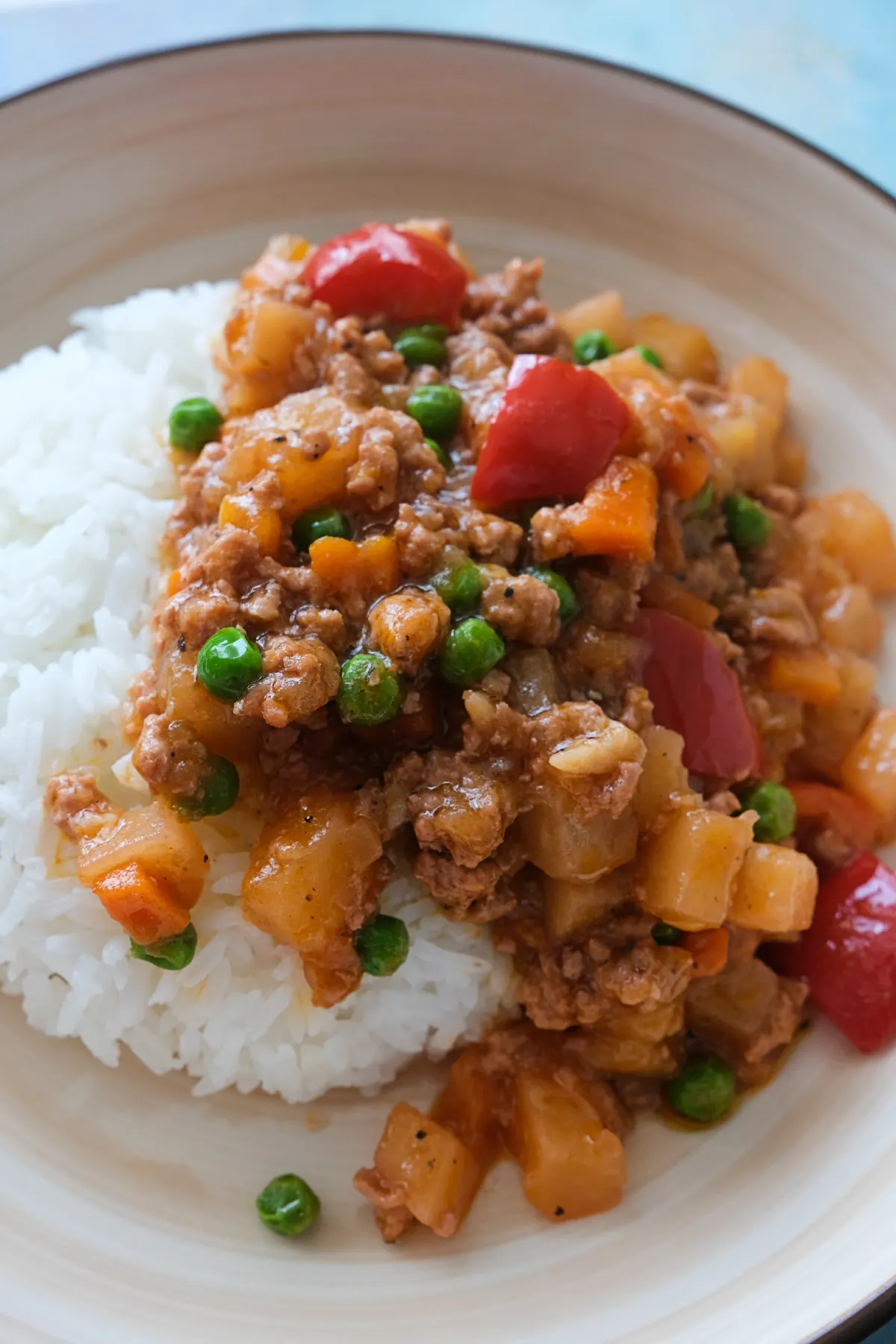 Ground pork picadillo with potatoes, carrots, peas, and red bell peppers spooned over steamed rice.