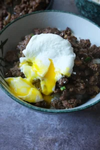 Bowl of rice topped with bulgogi ground beef and a soft poached egg, served with chopsticks.