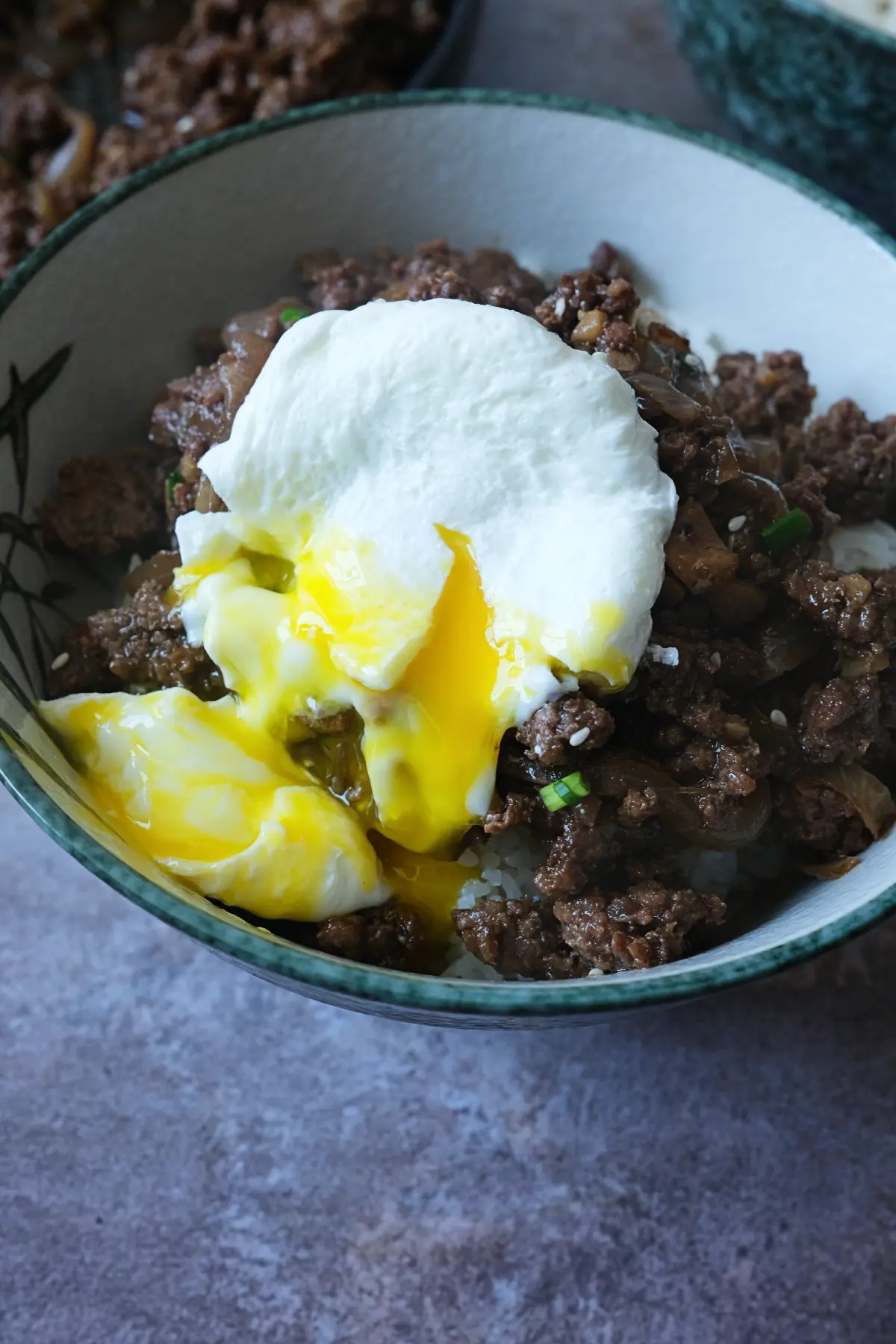 Close-up of ground beef bulgogi over rice with a soft poached egg, golden yolk flowing over the meat.