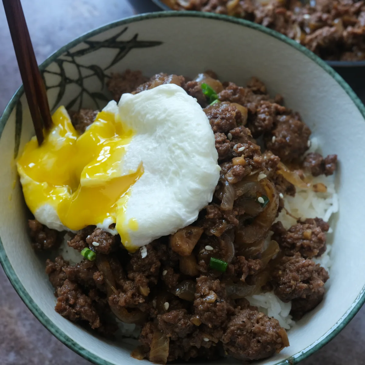 Runny poached egg breaking over ground beef bulgogi and rice in a bowl