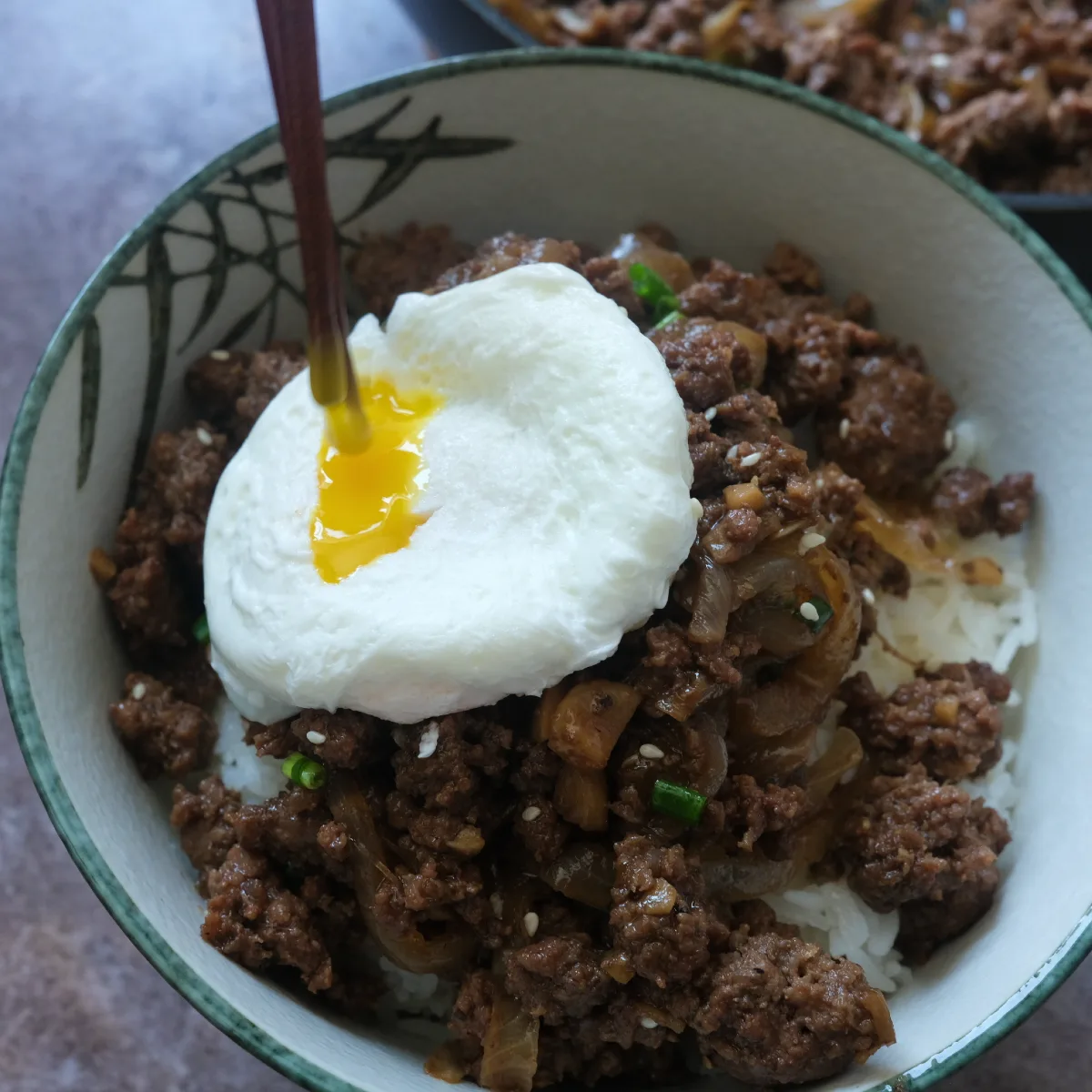 Runny poached egg breaking over ground beef bulgogi and rice in a bowl
