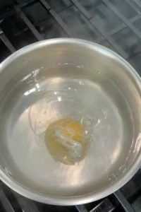 Perfectly poached egg resting on a strainer after cooking.