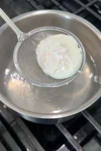 Perfectly poached egg resting on a strainer after cooking.