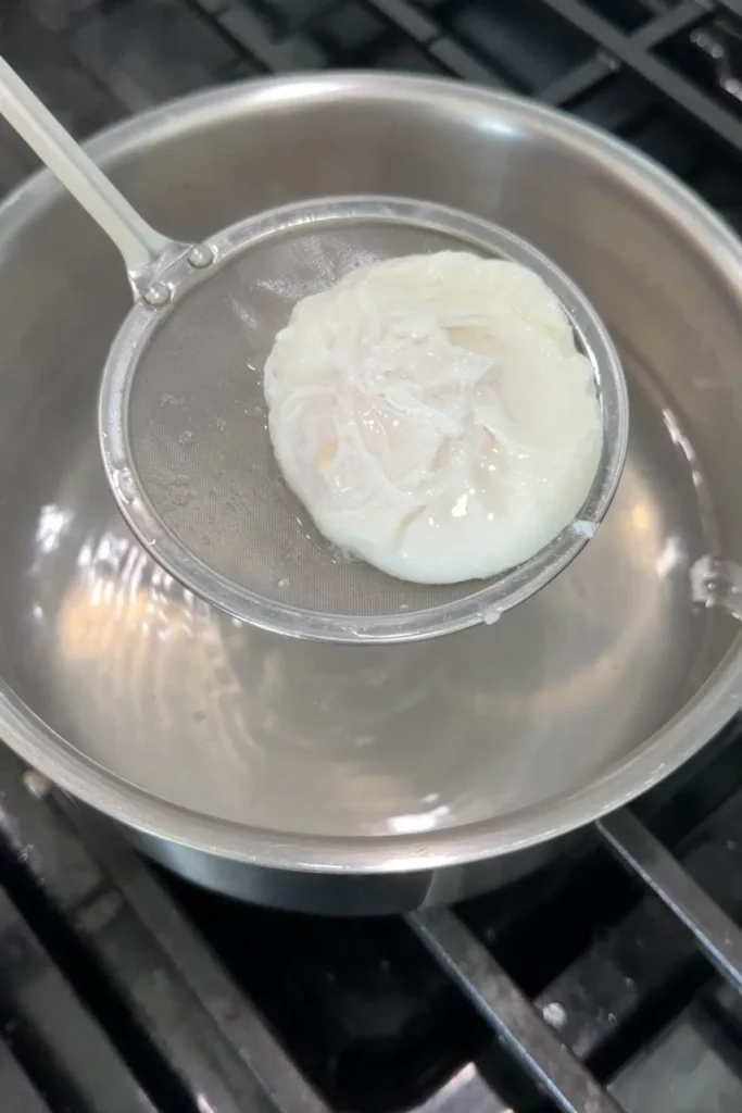 Perfectly poached egg resting on a strainer after cooking.