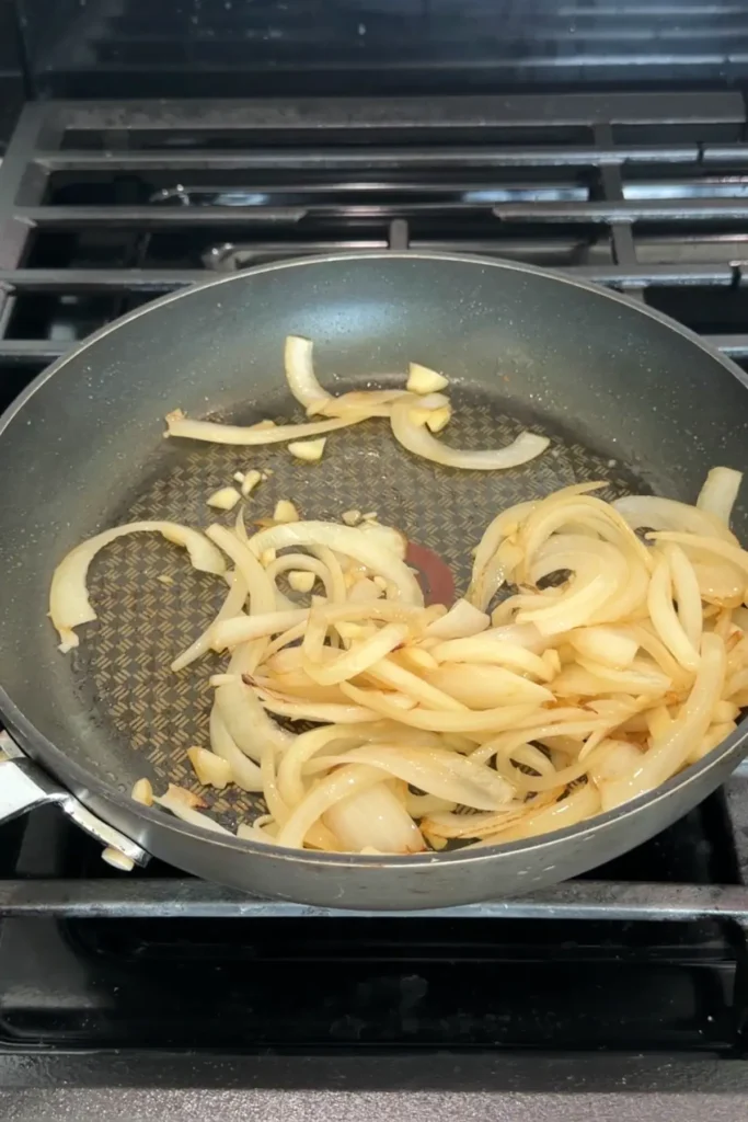 Sautéing sliced onions and garlic in a skillet until softened