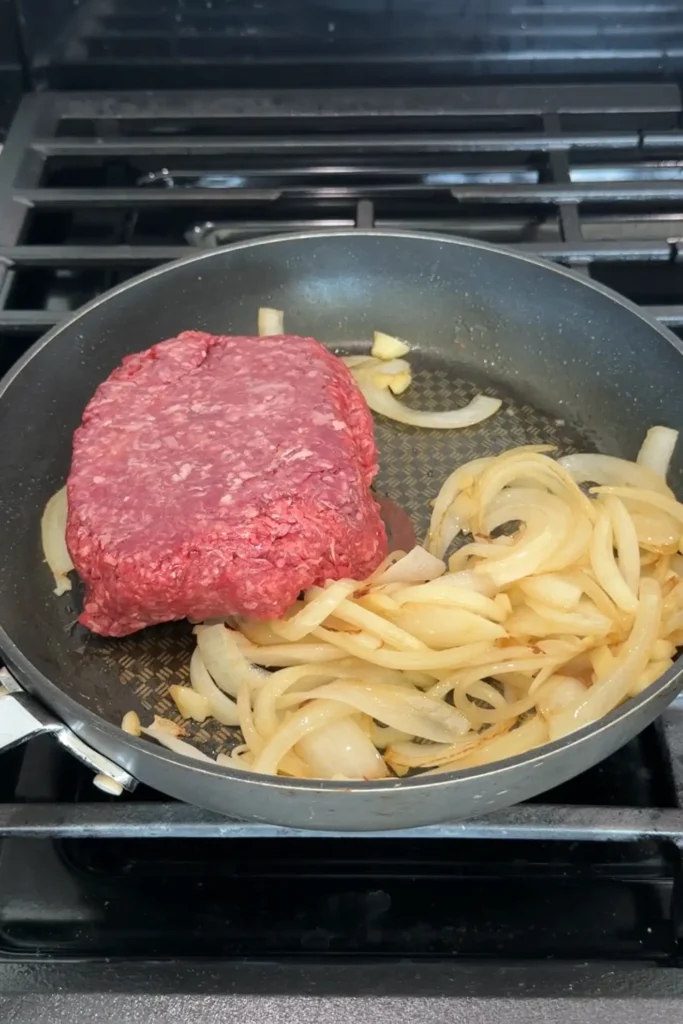 Raw ground beef added to sautéed onions and garlic in a skillet.