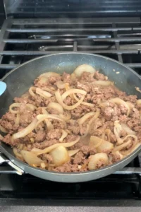 Ground beef cooking with onions and garlic, breaking apart and browning.