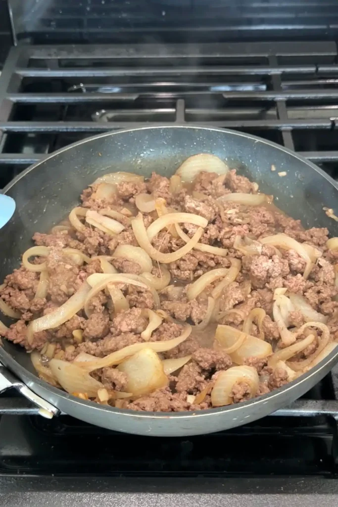 Ground beef cooking with onions and garlic, breaking apart and browning