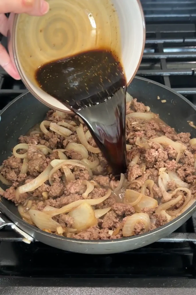 Sweet and savory bulgogi sauce being poured over cooked ground beef and onions.