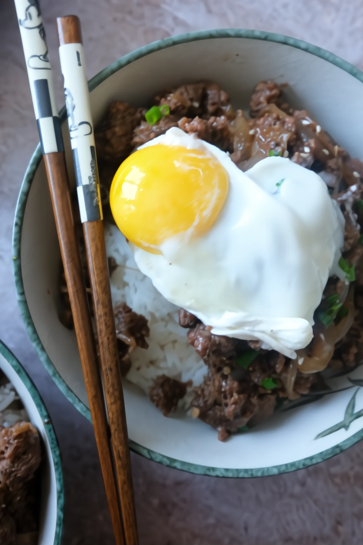 Ground beef bulgogi rice bowl topped with a soft poached egg, served with chopsticks and garnished with green onions.