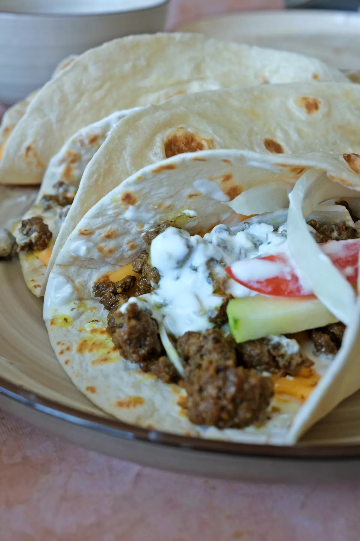 Close-up of assembled shawarma wraps with visible melted cheese, seasoned beef, cucumber, tomato, onion, and yogurt sauce