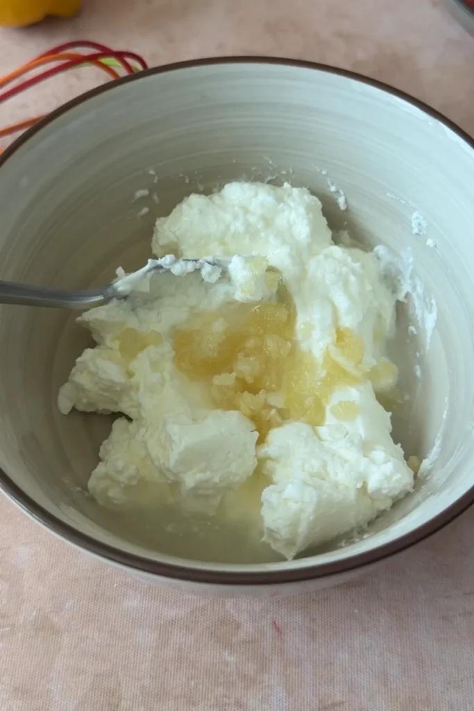Thick yogurt in a bowl combined with minced garlic and lemon juice, partially mixed with visible chunks.