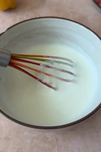 Creamy yogurt garlic sauce whisked until smooth in a bowl, with a whisk resting inside.