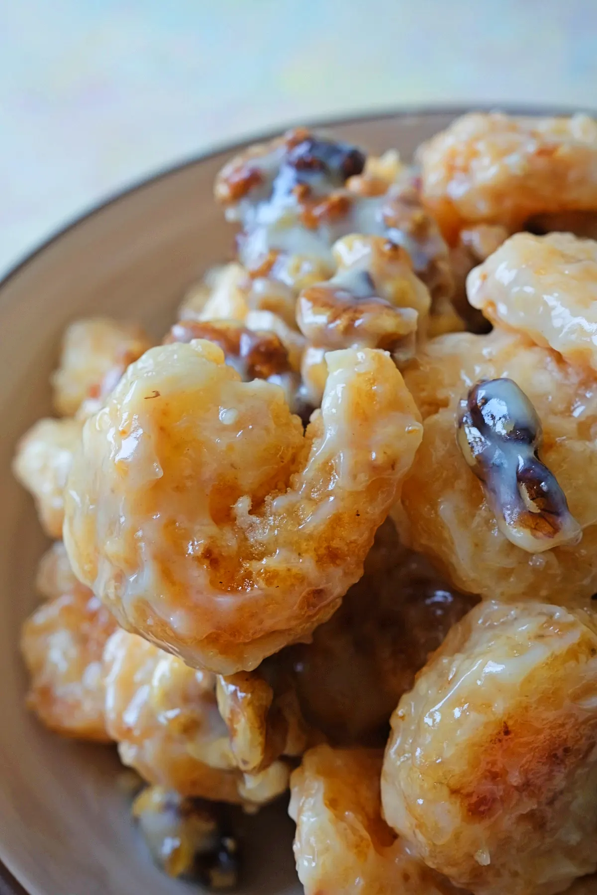 Tight close-up of a single honey walnut shrimp showing its craggy crispy coating covered in thick, glossy white sauce with caramelized walnuts in the background.