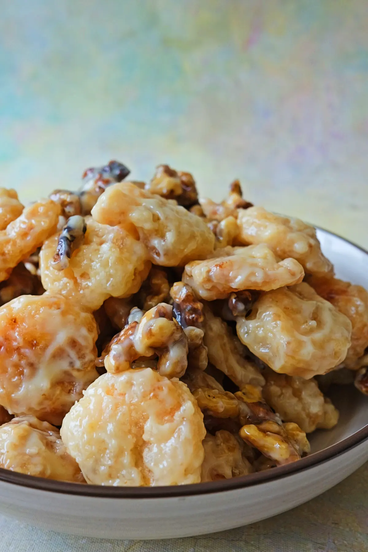 Side angle of a plate piled with honey walnut shrimp, highlighting the creamy glaze clinging to each golden piece with walnuts tucked between.
