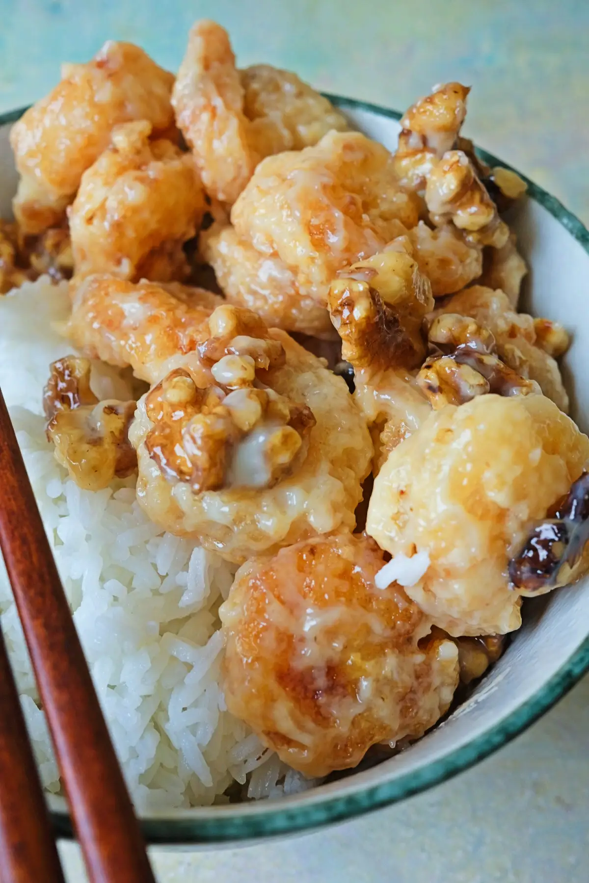 Honey walnut shrimp served over white rice in a ceramic bowl, with chopsticks resting on the side and sauce dripping onto the rice below.