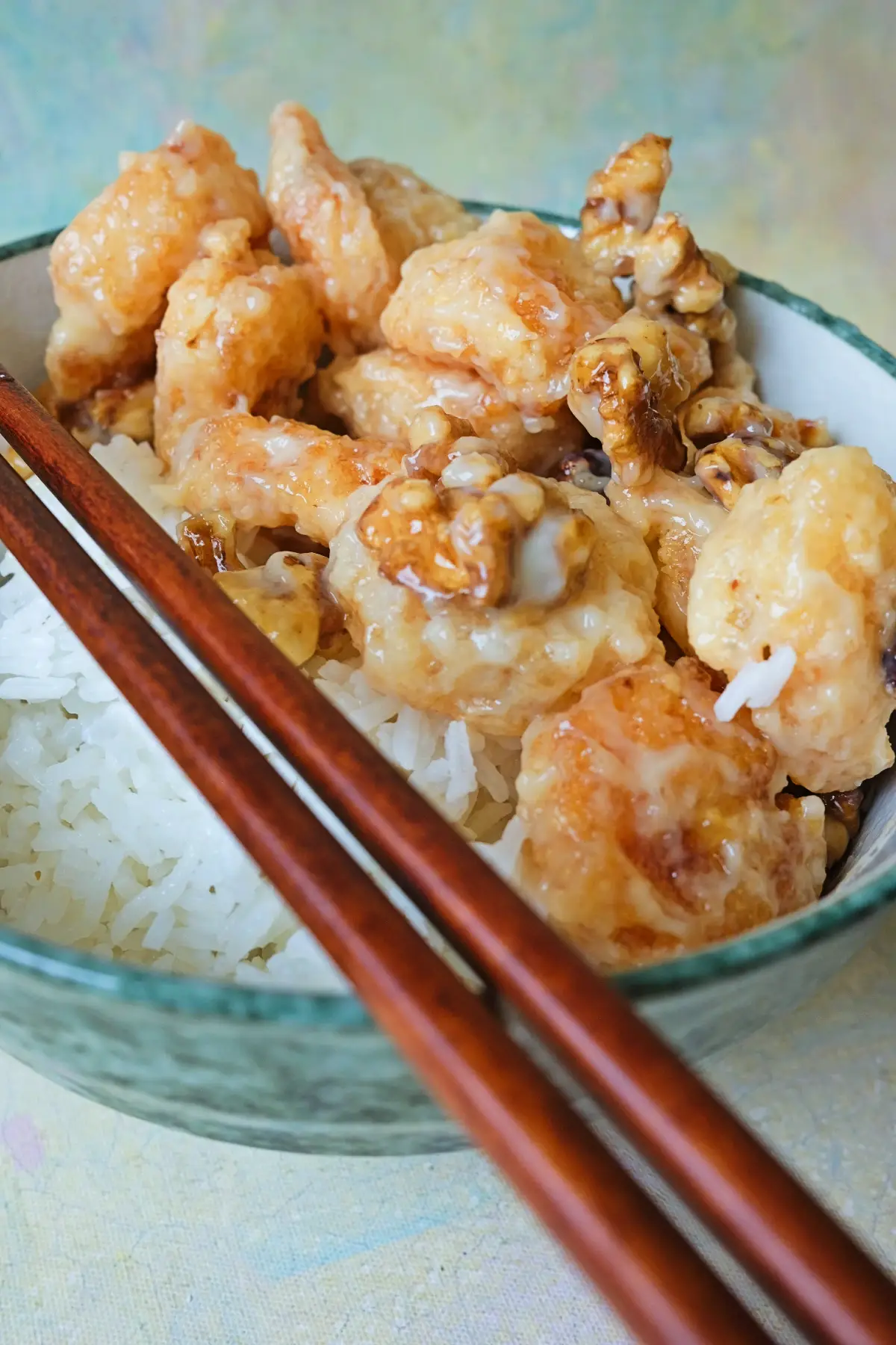 Honey walnut shrimp over steamed white rice with wooden chopsticks placed across the bowl, showing contrast between fluffy rice and crispy coated shrimp.