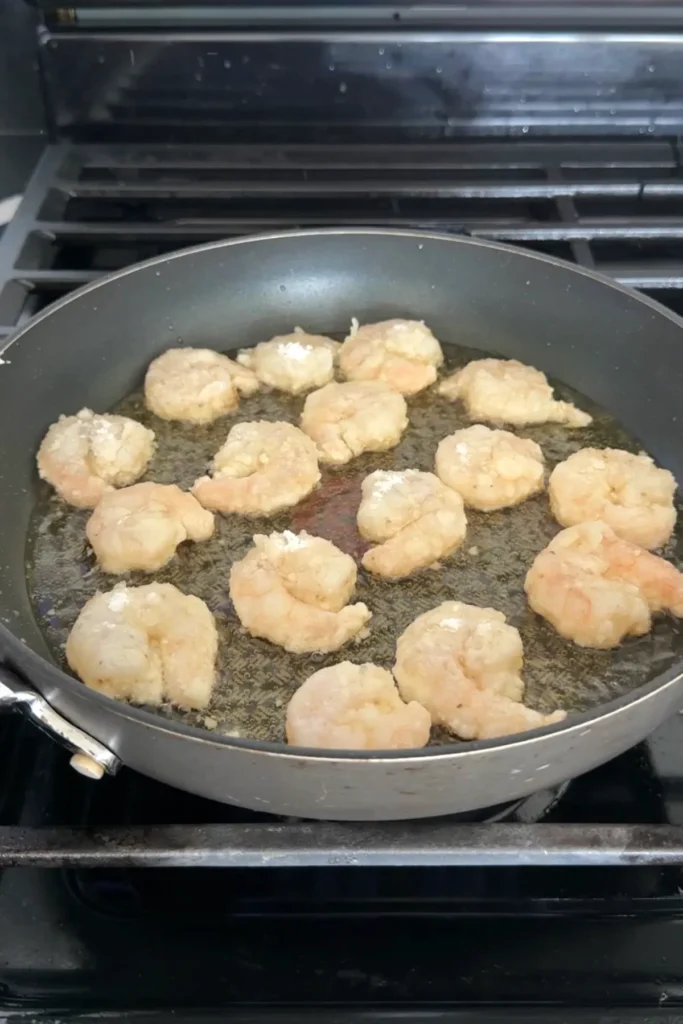 Shrimp frying in hot oil in a pan, lightly coated and beginning to turn golden