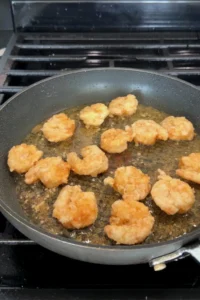 Shrimp frying in oil turning golden brown and crispy on the stovetop