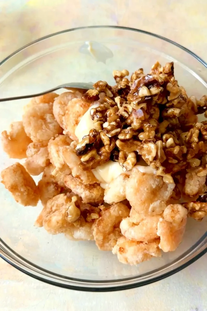 Fried shrimp topped with creamy sauce and candied walnuts in a glass bowl