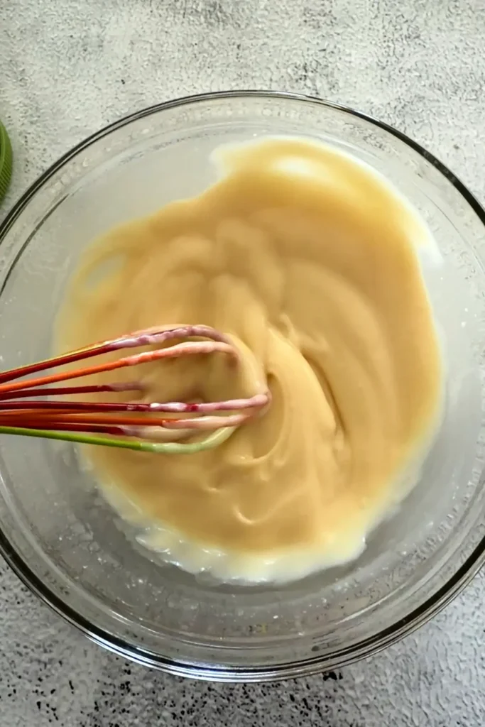 Whisking mayonnaise and honey together in a glass bowl until smooth and creamy sauce forms