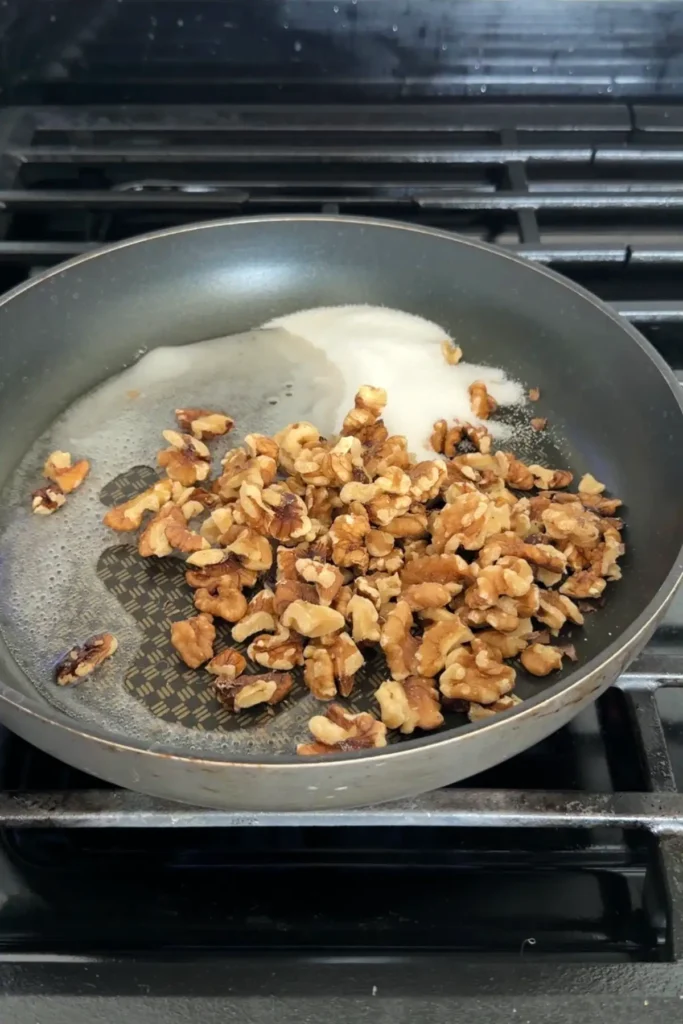 Chopped walnuts and sugar melting in a nonstick pan over a stovetop before caramelizing