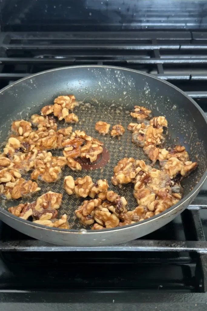 Walnuts coated in bubbling sugar syrup as they begin to caramelize in a skillet