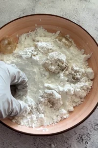 Shrimp being dredged in cornstarch or flour coating by hand in a shallow bowl