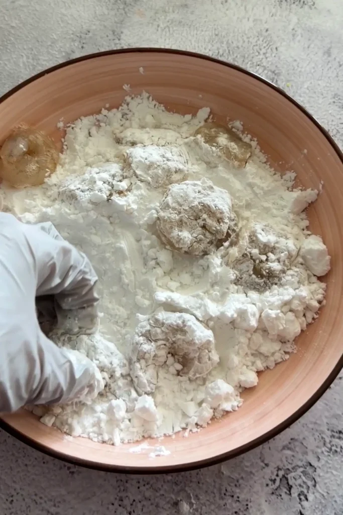 Shrimp being dredged in cornstarch or flour coating by hand in a shallow bowl