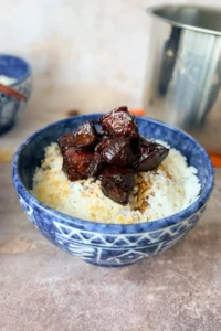 Chinese red braised pork belly served over white rice in a blue bowl