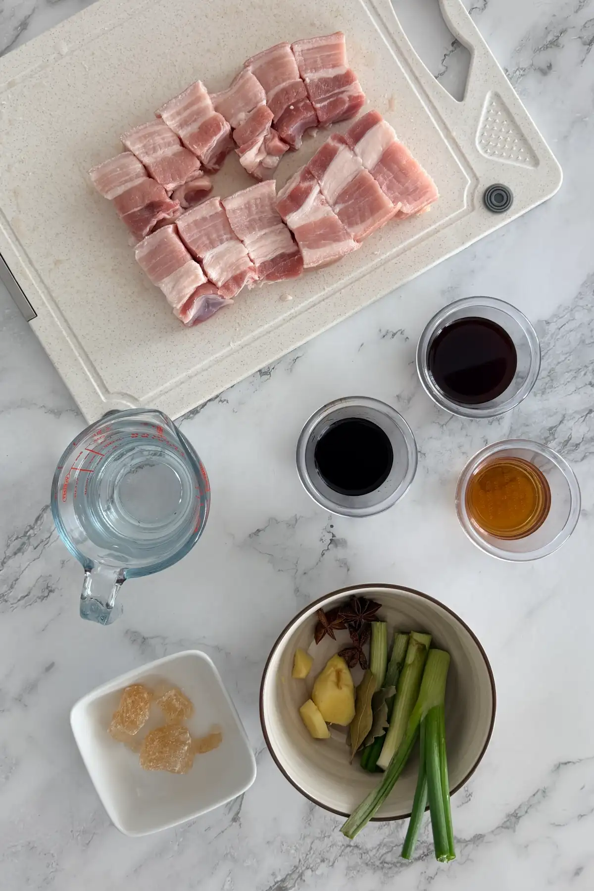 Raw pork belly cubes and ingredients for Hong Shao Rou on a cutting board