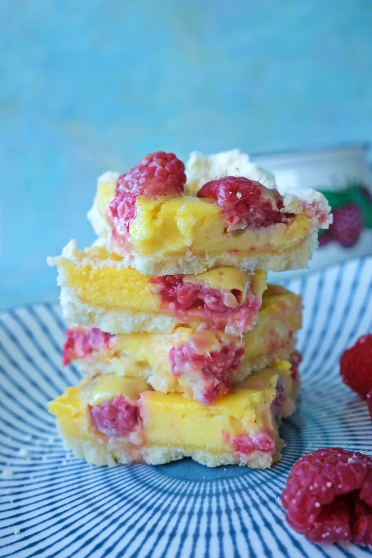 Stacked raspberry lemon bars on a plate showing the creamy lemon layer and raspberries inside.