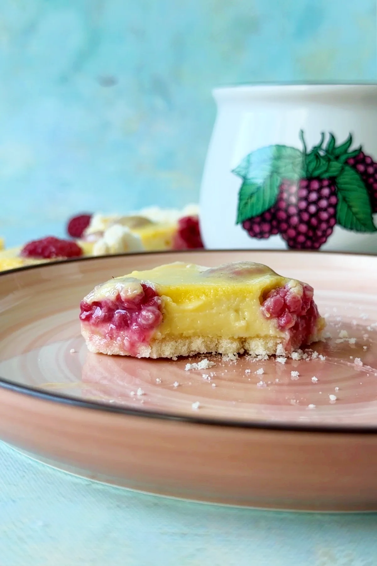 Single raspberry lemon bar topped with fresh raspberries on a dessert plate.