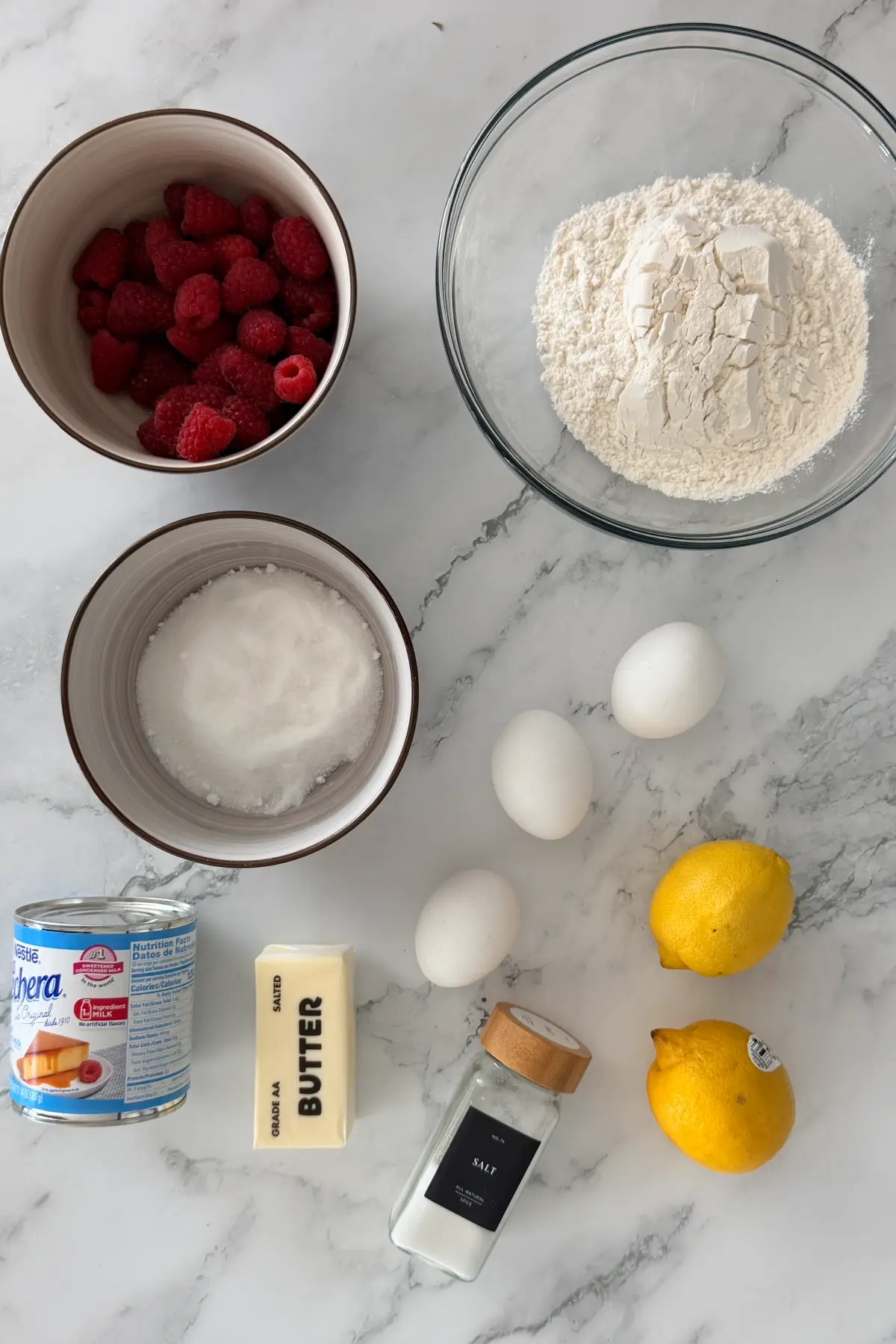 Ingredients for raspberry lemon bars including raspberries, lemons, flour, eggs, butter, and condensed milk.