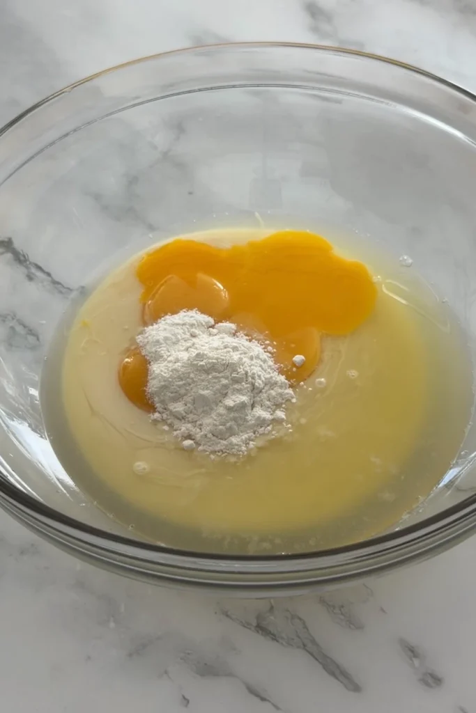 Egg yolks, condensed milk, lemon juice, and flour in a bowl for raspberry lemon bar filling.