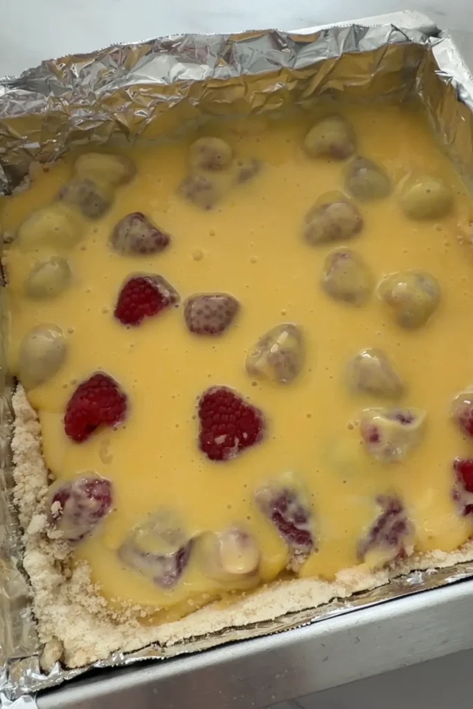 Unbaked raspberry lemon bars with raspberries in lemon filling over shortbread crust.