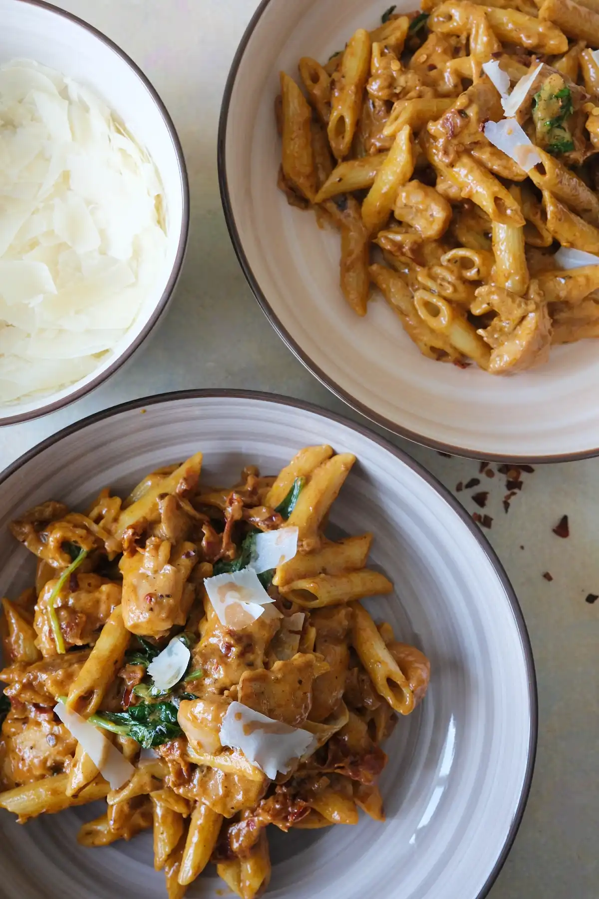 Two bowls of marry me chicken pasta with parmesan shavings and sun-dried tomatoes on a table.