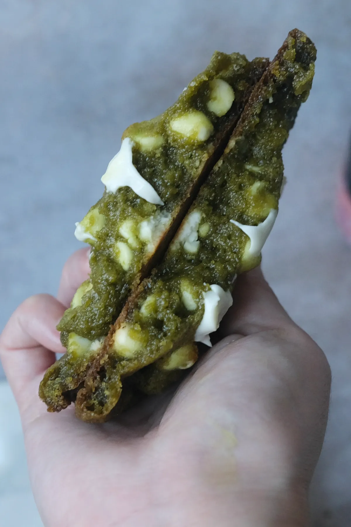 Close-up of a matcha white chocolate cookie broken in half with a chewy center and melted white chocolate.