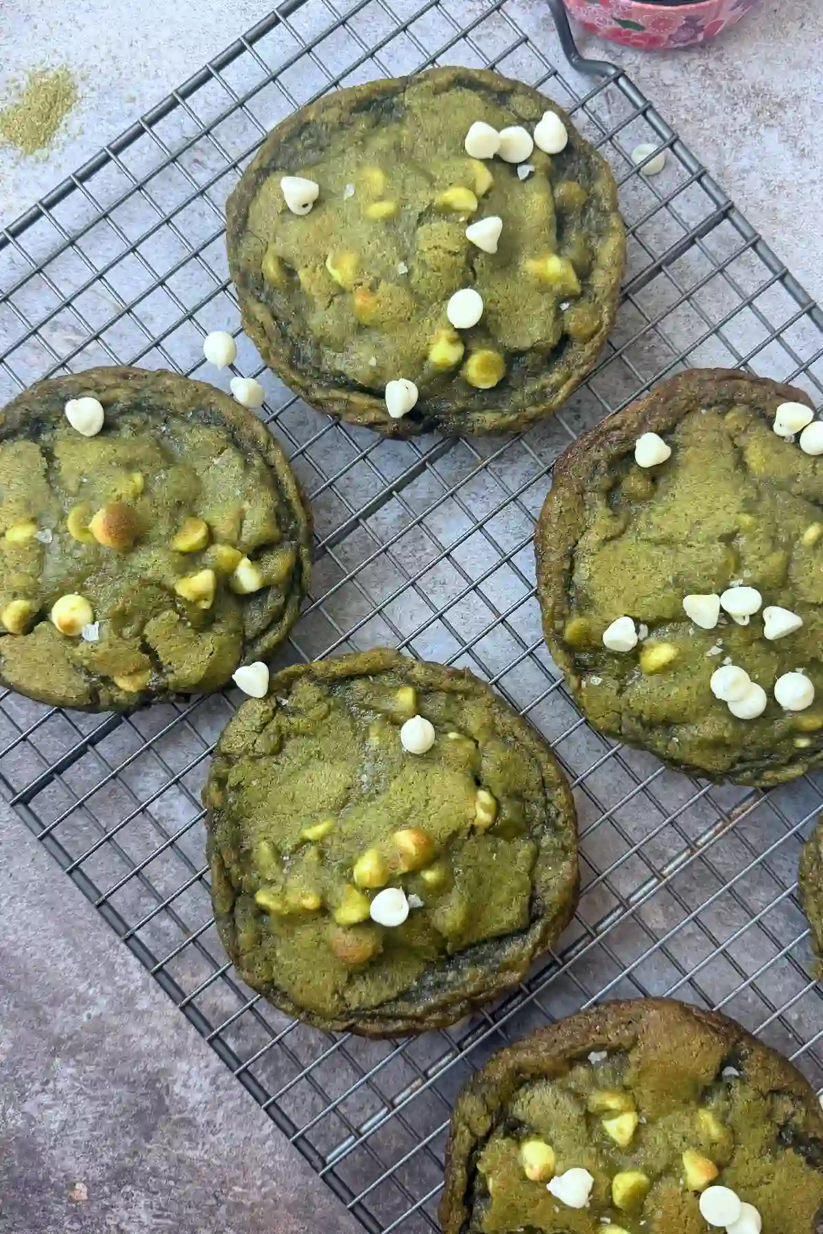 Overhead view of matcha white chocolate cookies on a cooling rack with white chocolate chips and flaky salt.