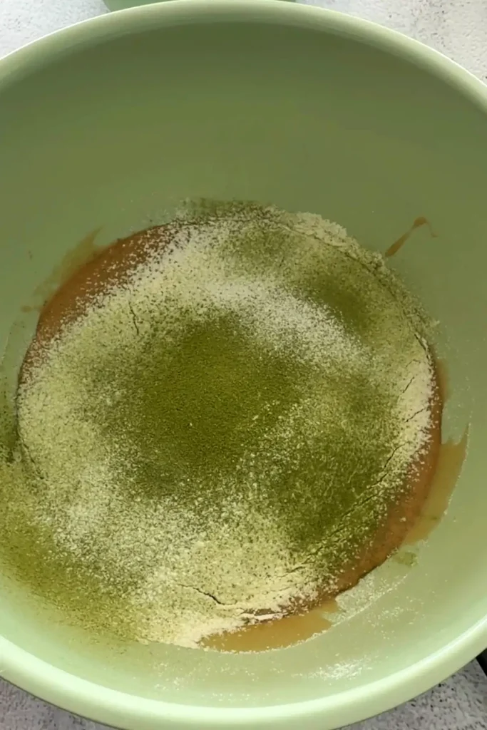 Sifted dry ingredients added over the wet ingredients in a mixing bowl.