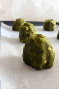 Tall mounds of matcha white chocolate cookie dough shaped on a parchment-lined baking sheet.