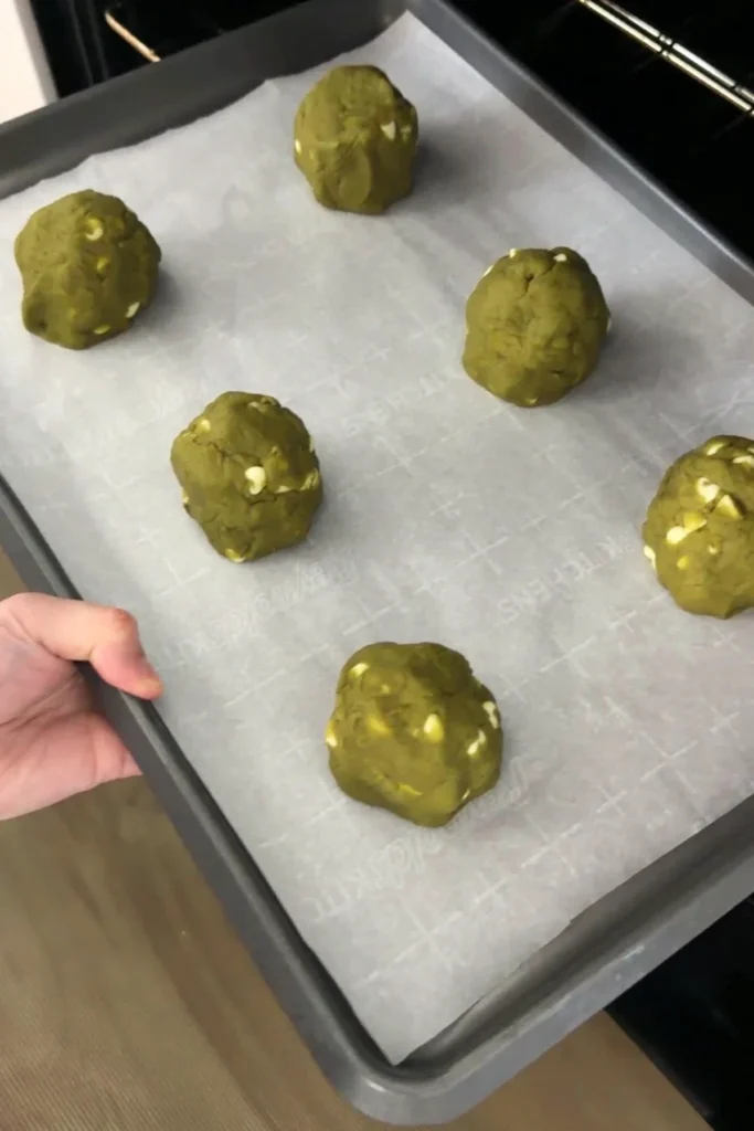 Chilled matcha white chocolate cookie dough mounds arranged on a parchment-lined baking sheet before baking.