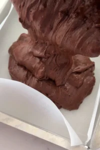 Pouring thick fudgy brownie batter into parchment-lined baking pan