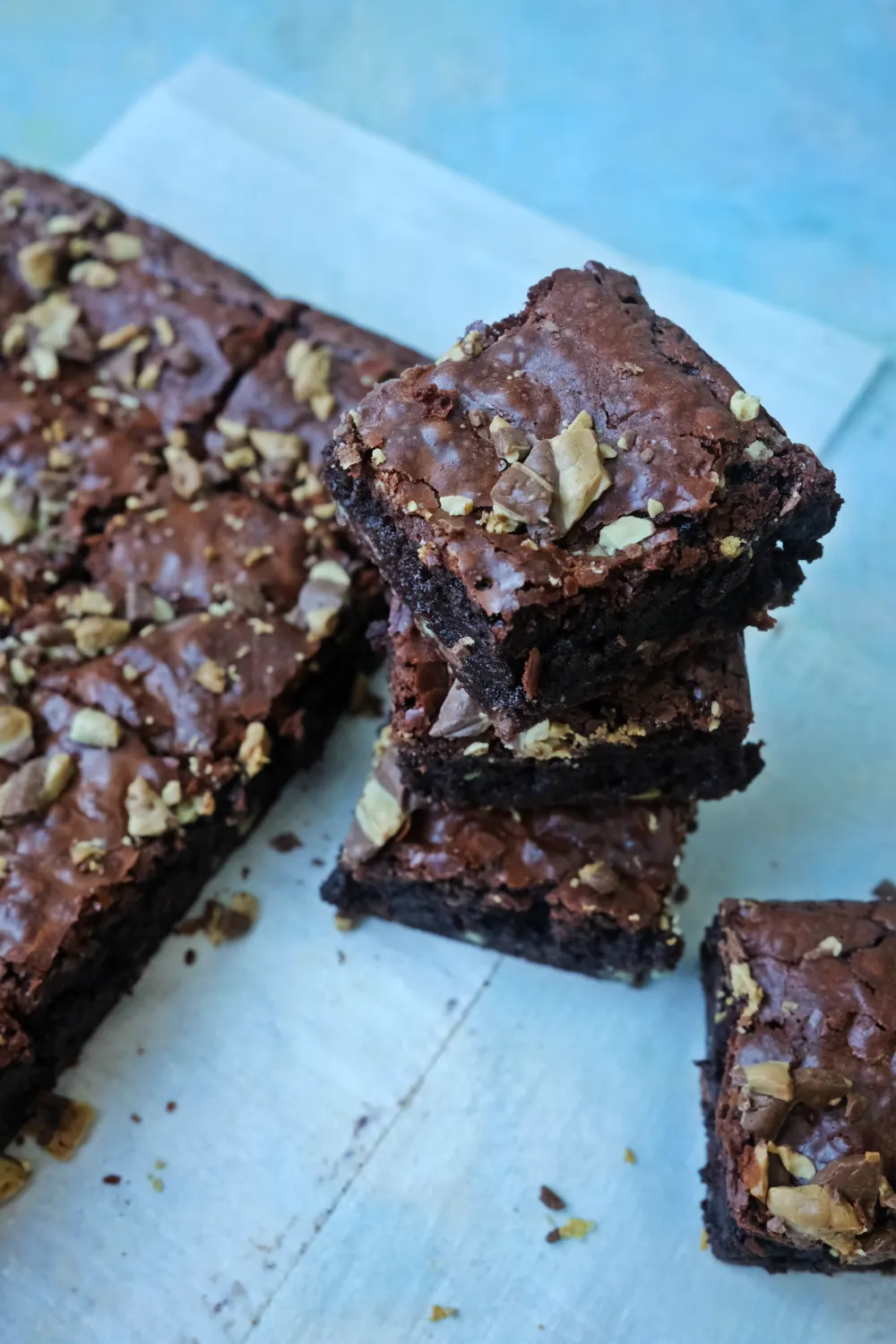Stack of fudgy mint chocolate chip brownie squares with crackly tops and chopped chocolate pieces on parchment-lined surface