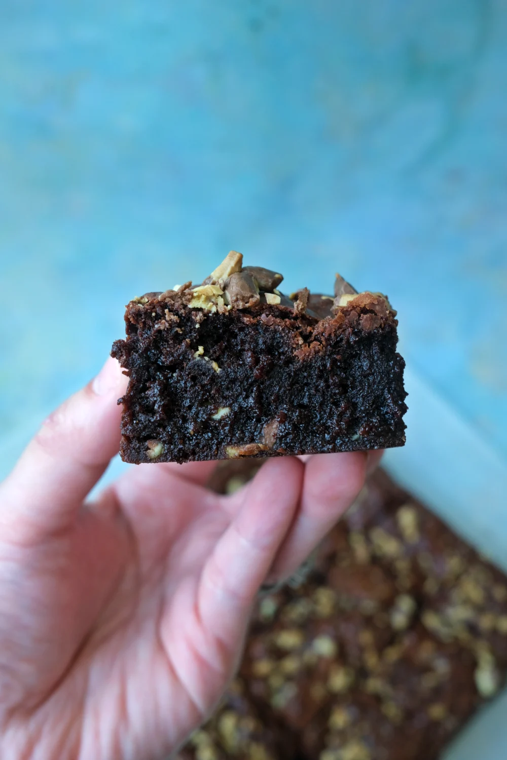 close up shot - Hand holding a fudgy brownie showing moist interior and melted chocolate bits